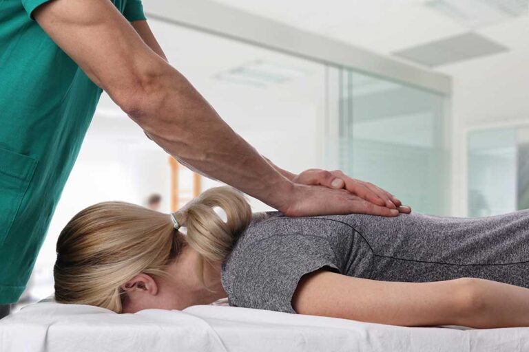 Chiropractor discussing a spine model with an adult patient in a quiet examination room.